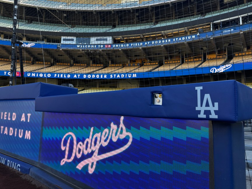 Screens behind home plate with Dodger blue cushioned padding with small rectangular cutouts custom-sized for the iPhone 18 Pro Max's cameras. 