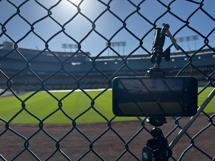 A phone mounted to a tripod behind a fence looking from the bullpen onto the field.