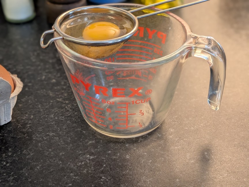 egg in strainer above measuring cup