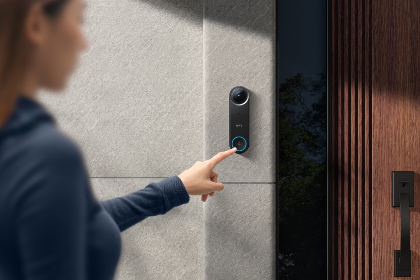 Person reaching out to black Eufy doorbell on trim.