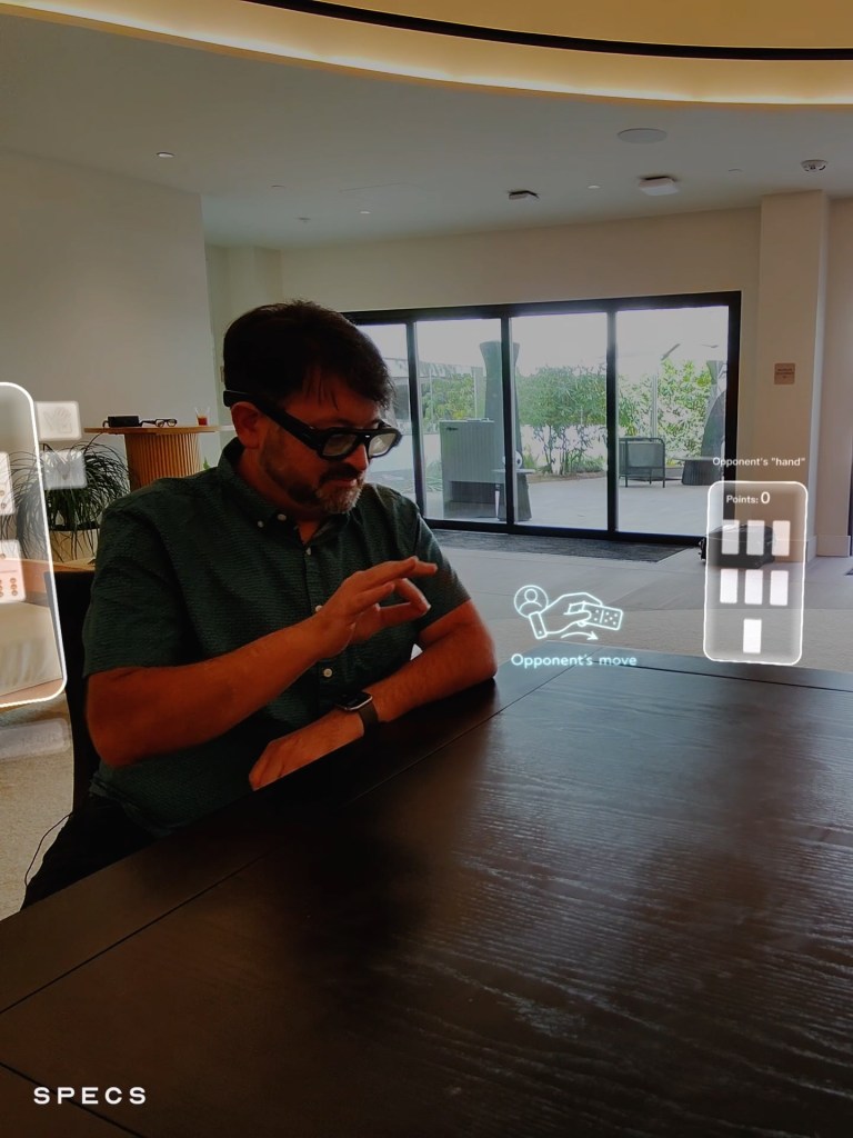 Scott Stein playing virtual dominoes with Specs glasses on, showing virtual game layers in the world around him