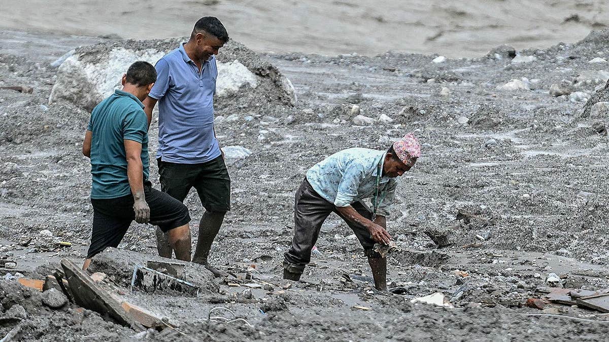Employees retrieve banknotes near a sludge-covered bank in Trishuli, Nepal.