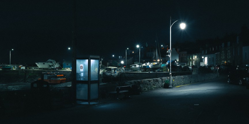Image of a street at night. A phonebox is lit up.